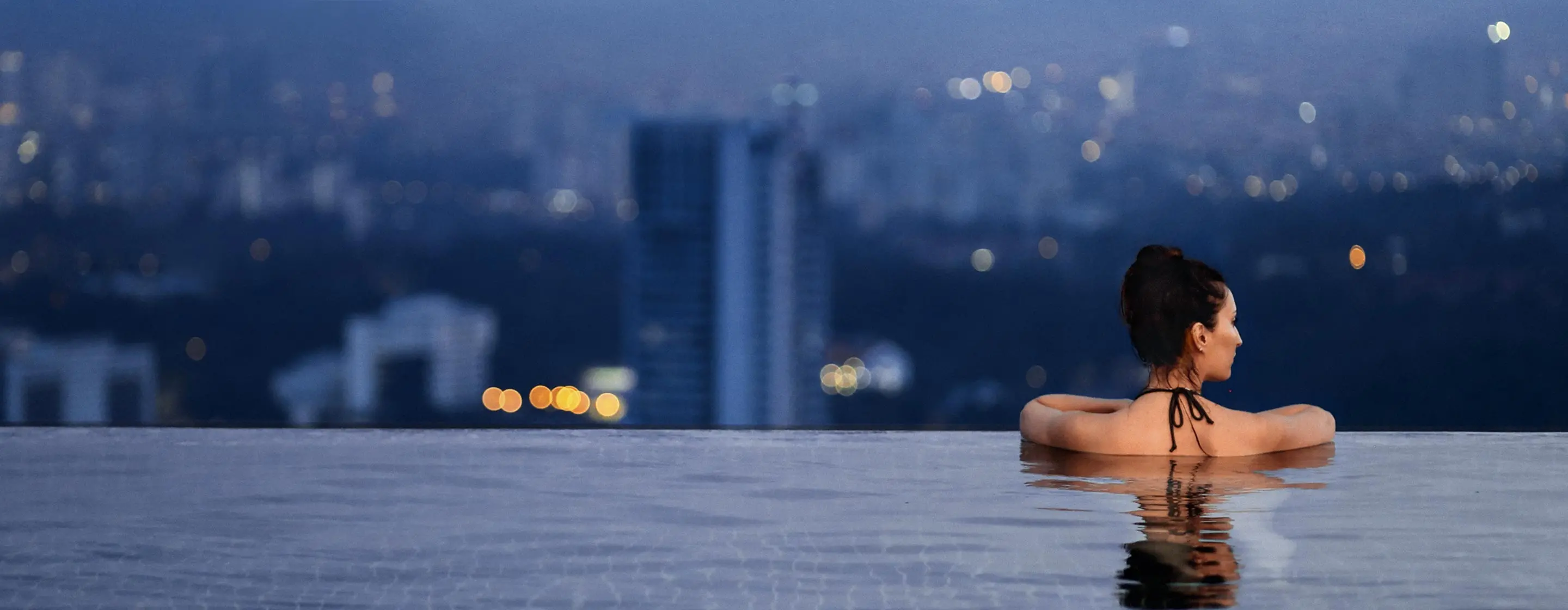 Frau blickt von Infinity-Pool aus in Richtung Hochhaus-Skyline