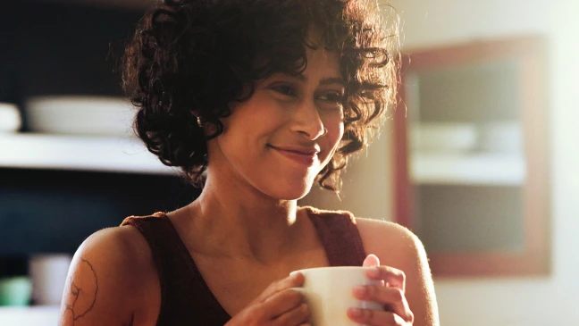 Person hält eine helle Tasse mit beiden Händen. Das Bild zeigt einen unscharfen Innenraum im Hintergrund.