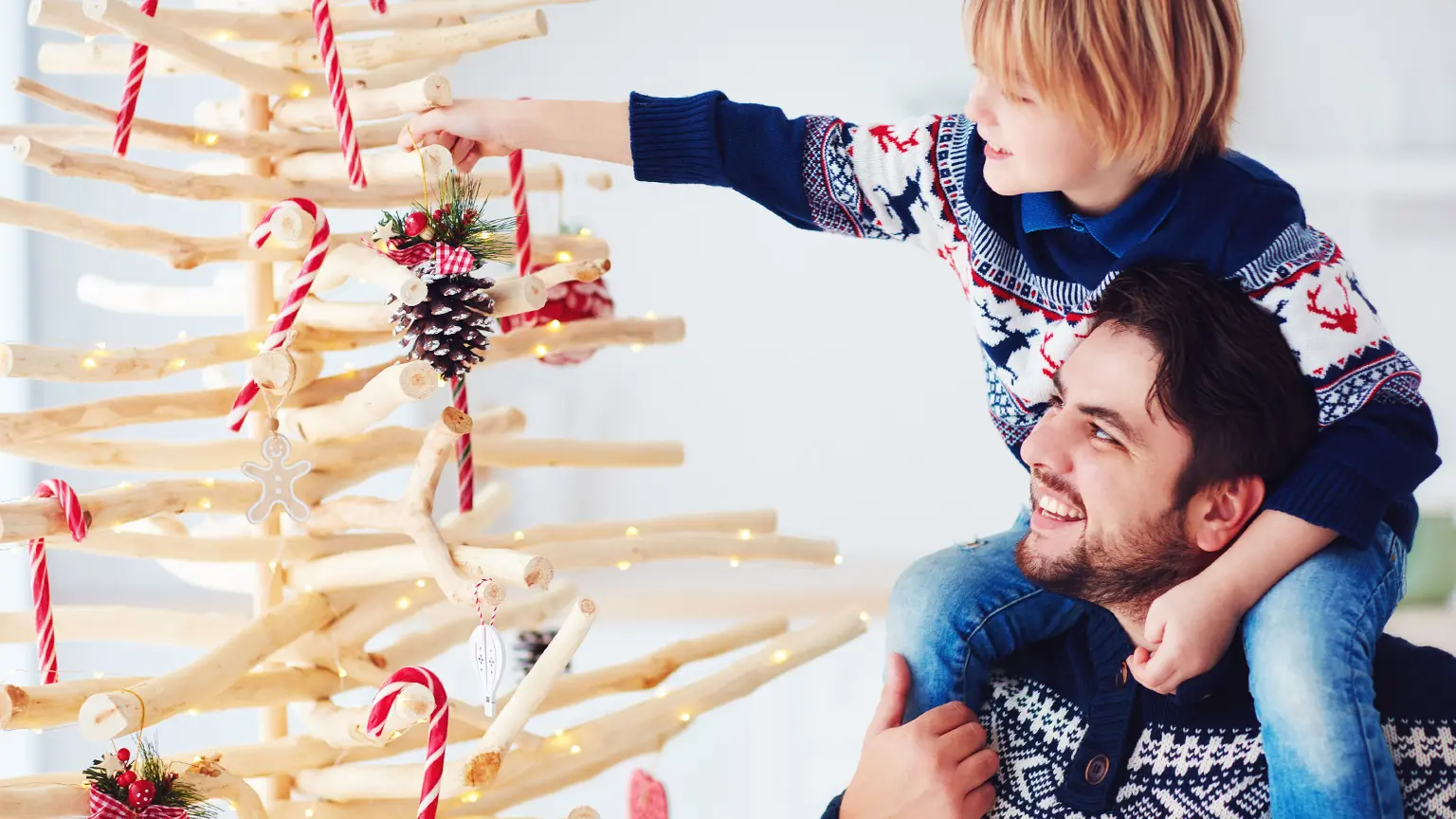 Person mit langen Haaren und rotem Oberteil sitzt an einem Tisch und schaut lächelnd auf einen Laptop vor einem Fenster.