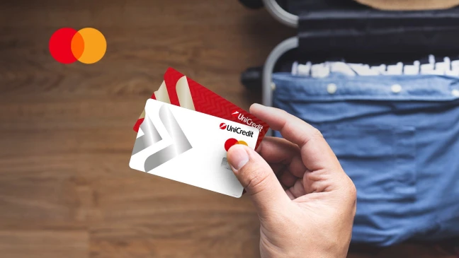 Hand hält UniCredit Karten vor geöffnetem Koffer auf Reisen