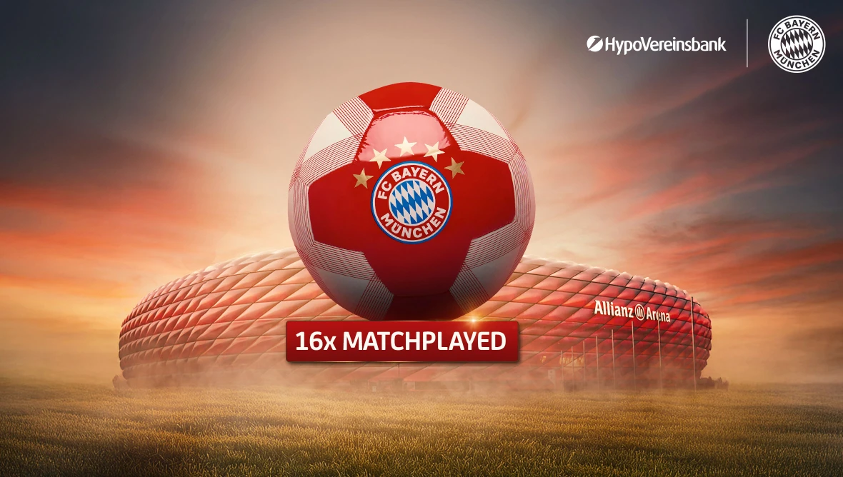 Matchplayed-Ball des FC Bayern München mit Sponsorenlogos, präsentiert vor der Allianz Arena bei Sonnenuntergang davor ein rot-weißer Fußball mit Vereinslogo.