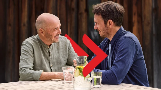 Christian und Felix Neureuther sitzen an einem Holztisch im Freien, vor ihnen Wasserkrug mit Zitronenscheiben und Gläser.