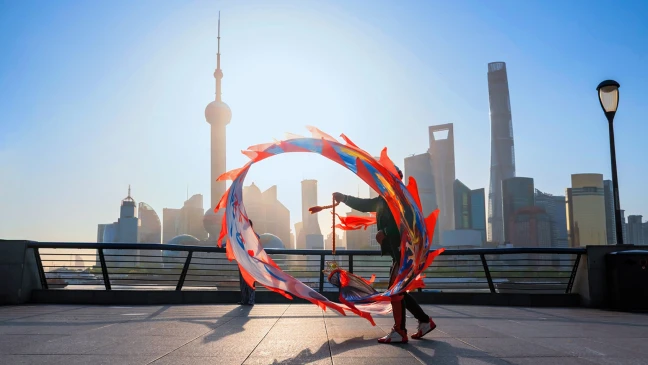 Person schwingt farbige Bänder auf einer Promenade mit Blick auf die Skyline von Shanghai bei Sonnenaufgang