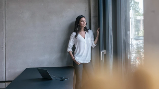 Frau vor grauer Wand am Fenster.