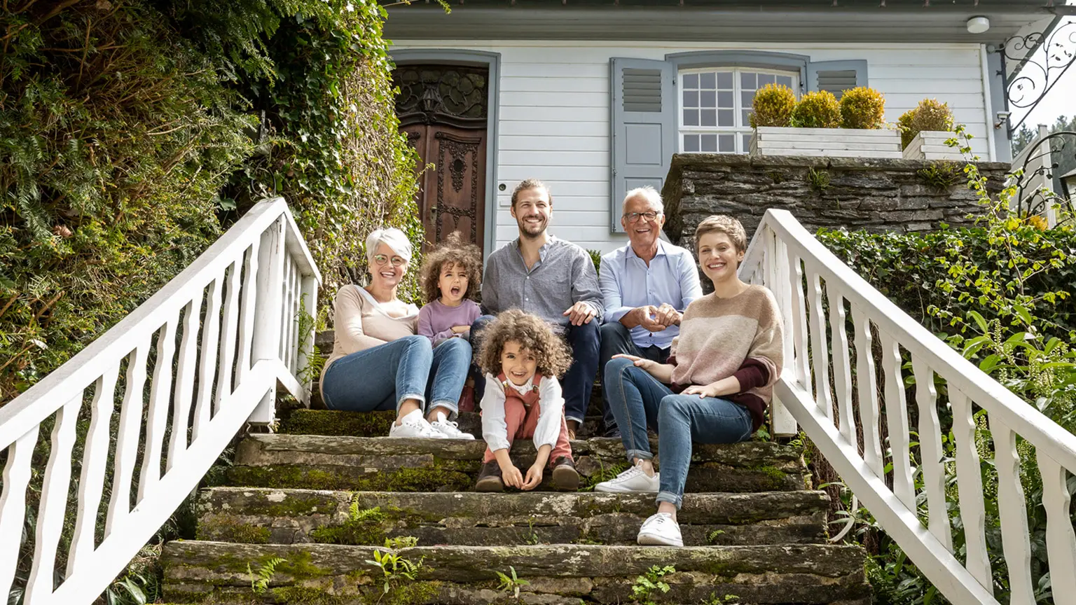 Mehrgenerationengruppe vor Wohnhaus im Grünen.