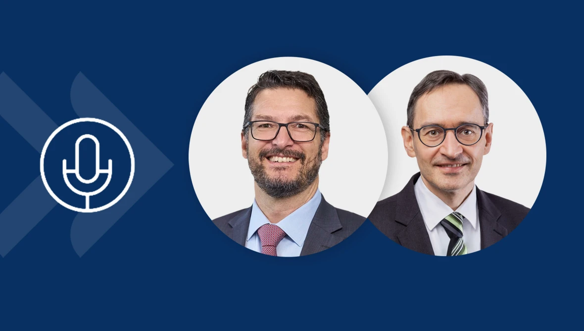 Drei Männer in formeller Kleidung stehen nebeneinander. Links ein glatzköpfiger Mann im dunklen Anzug mit weißem Hemd, in der Mitte ein Mann mit kurzen dunklen Haaren, Brille und hellem Hemd, rechts ein Mann mit kurzen dunklen Haaren, Bart, Brille und dunklem Anzug mit weißem Hemd. Links im Bild ist ein Mikrofon sichtbar.