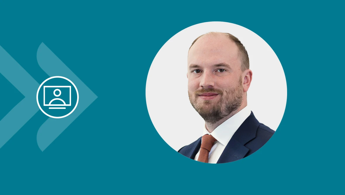 Eine geschäftlich gekleidete Person in kreisförmigem Portrait vor türkisfarbenem Hintergrund mit Video-Symbol.