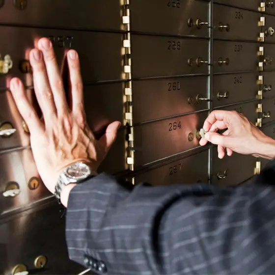 Person öffnet ein Schließfach in einer Metallwand mit nummerierten Fächern mithilfe eines Schlüssels während eine Hand auf einem anderen Fach liegt.