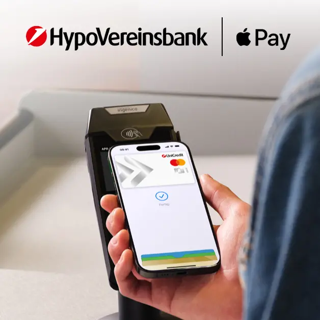 Person hält Smartphone an Kartenlesegerät neben Einkaufstasche, oben Logos von HVB und Apple Pay.