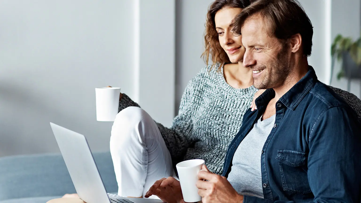Personen sitzen mit Laptop und Kaffeetassen im Wohnbereich.