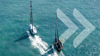 Eine Sicht von oben auf zwei Sport-Segelschiffe auf dem Wasser, ringsum ist nur Wasser zu sehen. Rechts sind zwei durchsichtige Pfeile als Icon auf dem Foto.