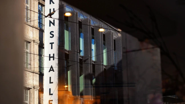 Ansicht einer Häuserzeile mit einem großem weißen Schild „KUNSTHALLE“ an einer Hausfassade und etwas verschwommenem Hintergrund.