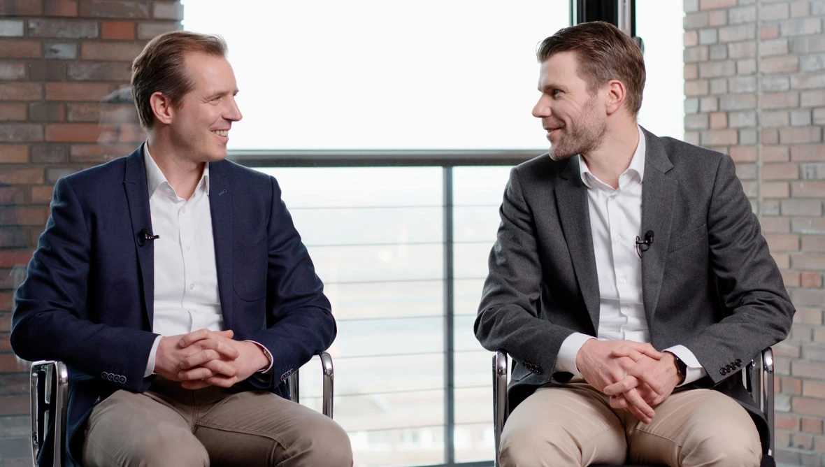 Zwei Männer im Business-Outfit sitzen sich in einem modernen Büro gegenüber.