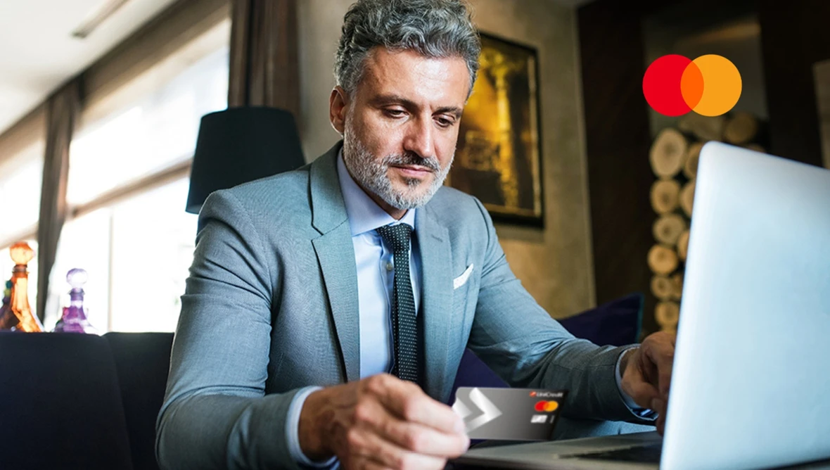 Person nutzt Mastercard beim Online-Einkauf am Laptop.