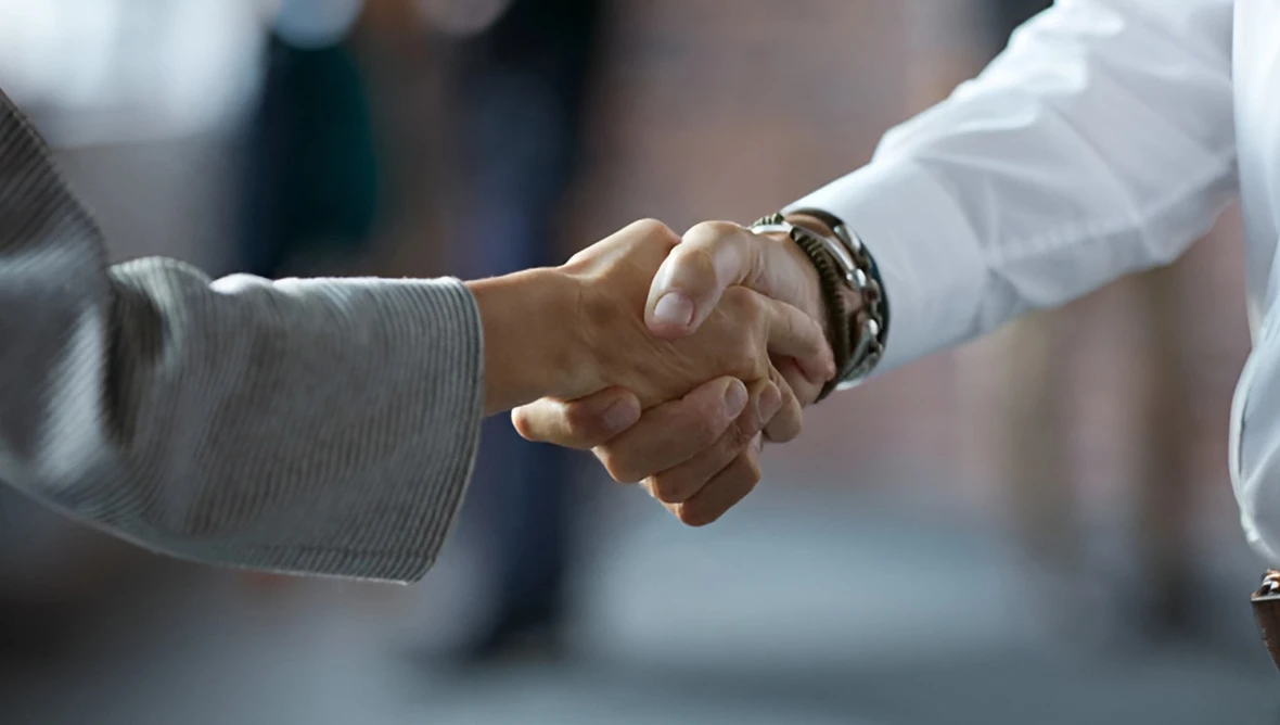 Zwei Personen geben sich die Hand, sichtbar sind nur die Hände im Vordergrund, der Hintergrund ist unscharf.