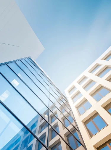 Zwei moderne Gebäude mit Glasfassade und weißen Fensterrahmen ragen in den blauen Himmel.
