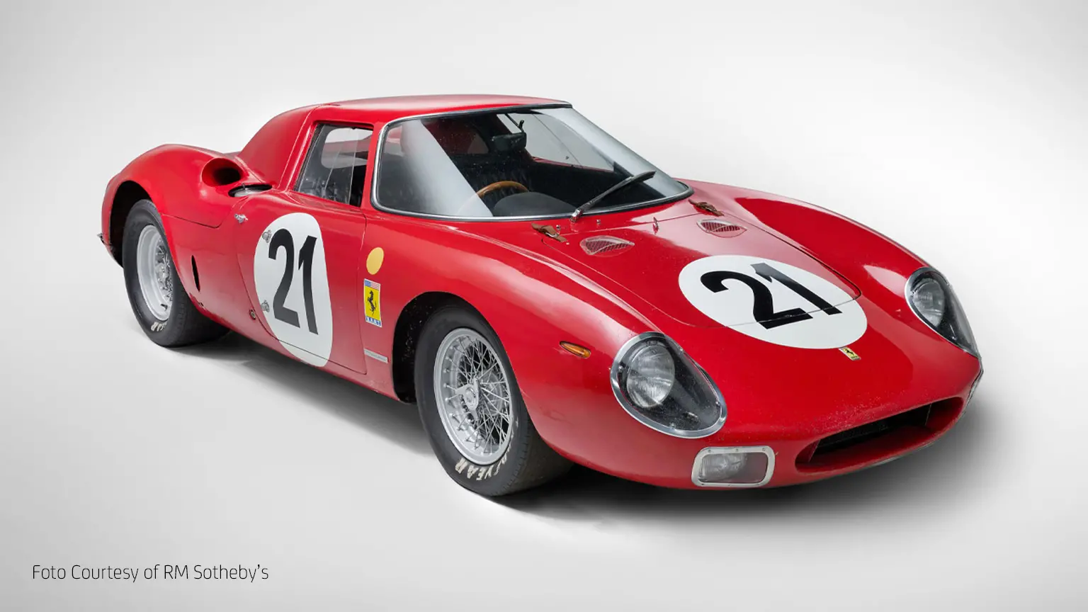 Roter historischer Ferrari-Rennwagen mit der Startnummer 21, seitlich und frontal fotografiert. Der Wagen hat ein aerodynamisches Design, runde Scheinwerfer, Speichenräder und ein Ferrari-Logo an der Seite. Unten links im Bild steht in kleiner Schrift: ‚Foto Courtesy of RM Sotheby’s‘.