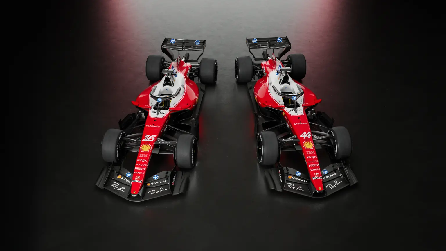 Zwei nebeneinander stehende Formel‑1-Rennwagen in Ferrari-Rot auf dunklem Untergrund, leicht von oben fotografiert. Beide Fahrzeuge zeigen schwarze Frontflügel, große Slickreifen und markante rote Lackierung mit Sponsorenlogos.