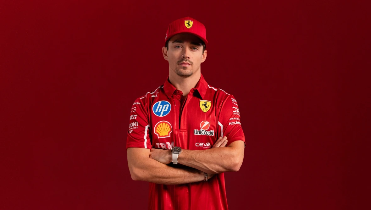 Person trägt ein rotes Ferrari-Teamshirt mit Sponsorenlogos wie Shell und HP sowie eine passende Ferrari-Cap, vor einem einfarbig roten Hintergrund.